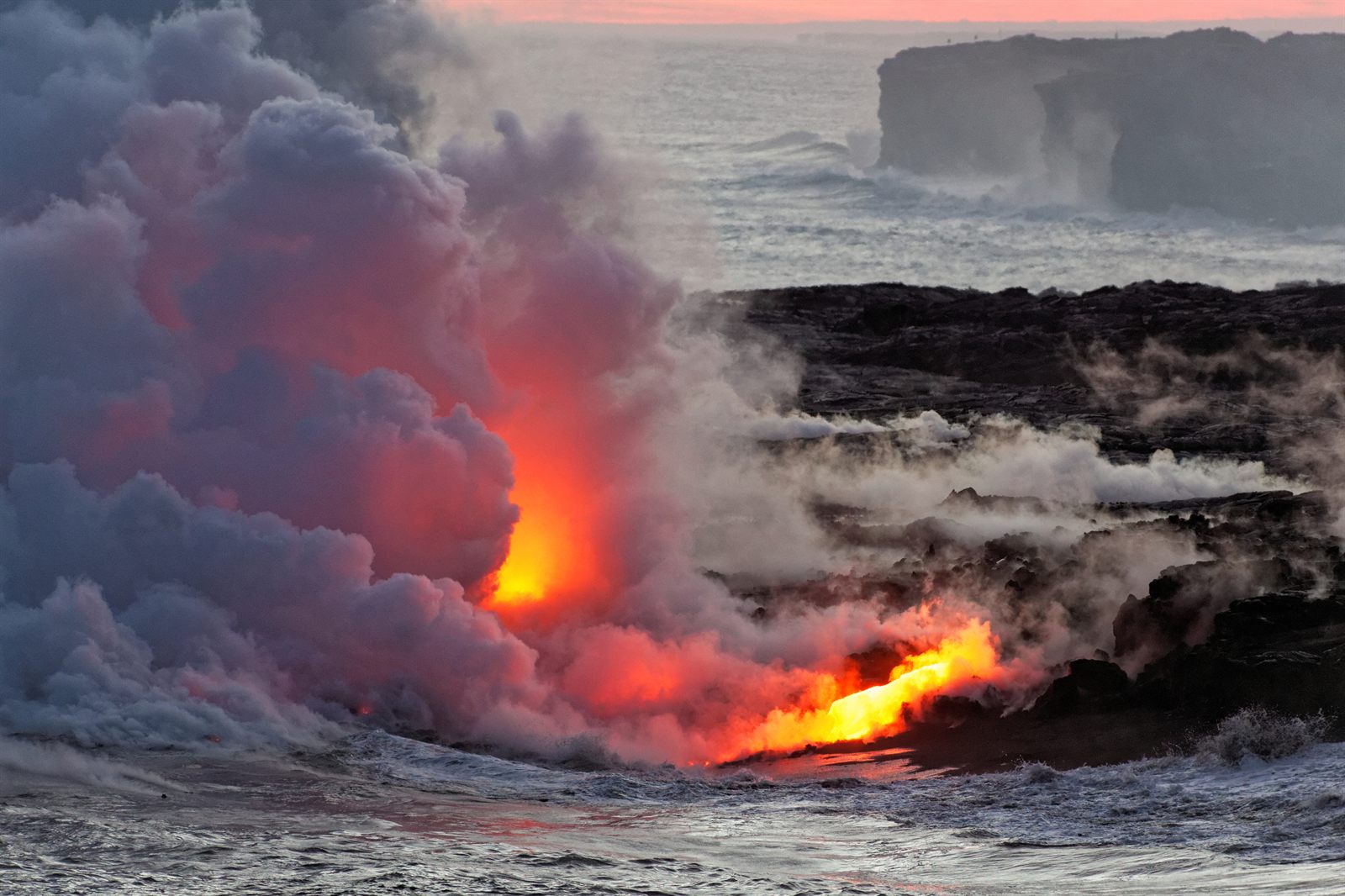 Glowing lava pouring into the ocean under clouds of steam on the island of Hawaii